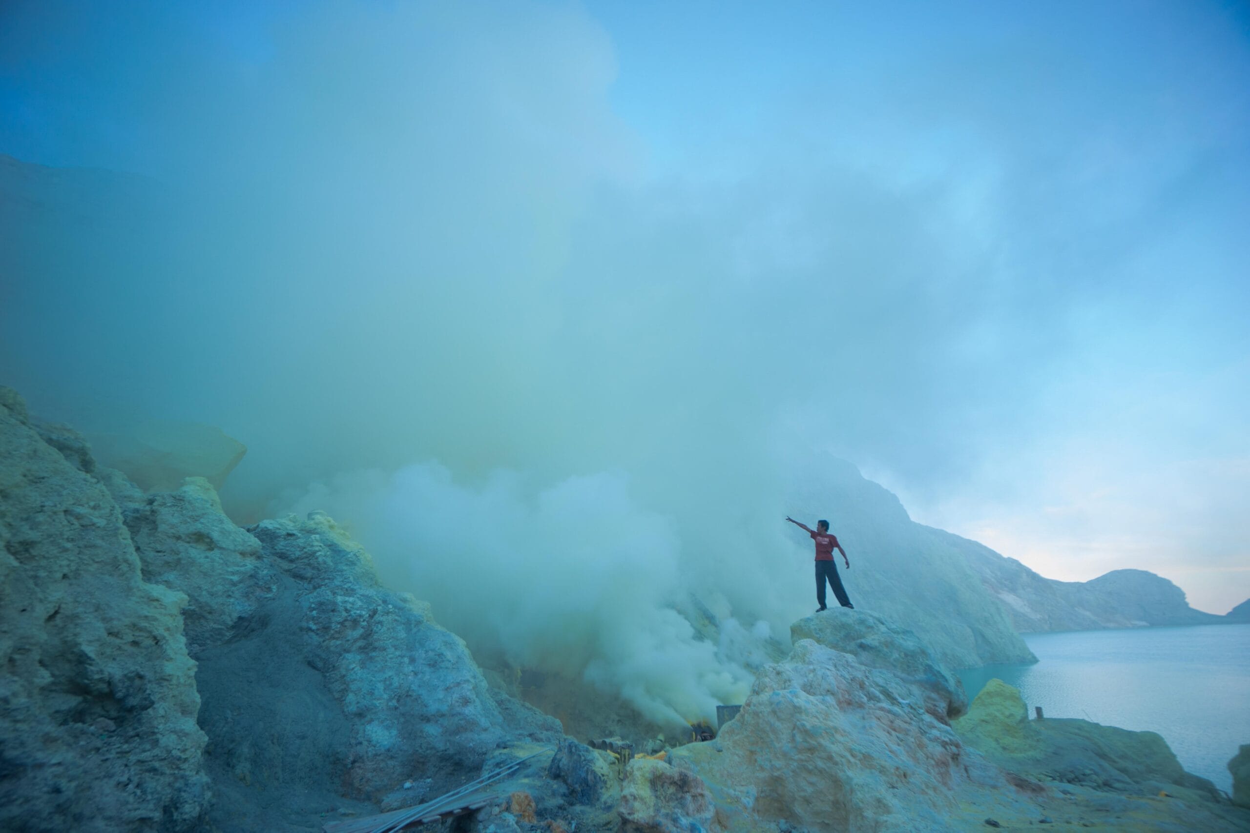 Hiker exploring sulfur clouds near the crater lake during Ijen sunrise & Blue Flame experience in East Java.