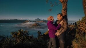 Couple enjoying sunrise view at Mount Bromo with mist-covered valley and volcano background during their Bromo Trip.