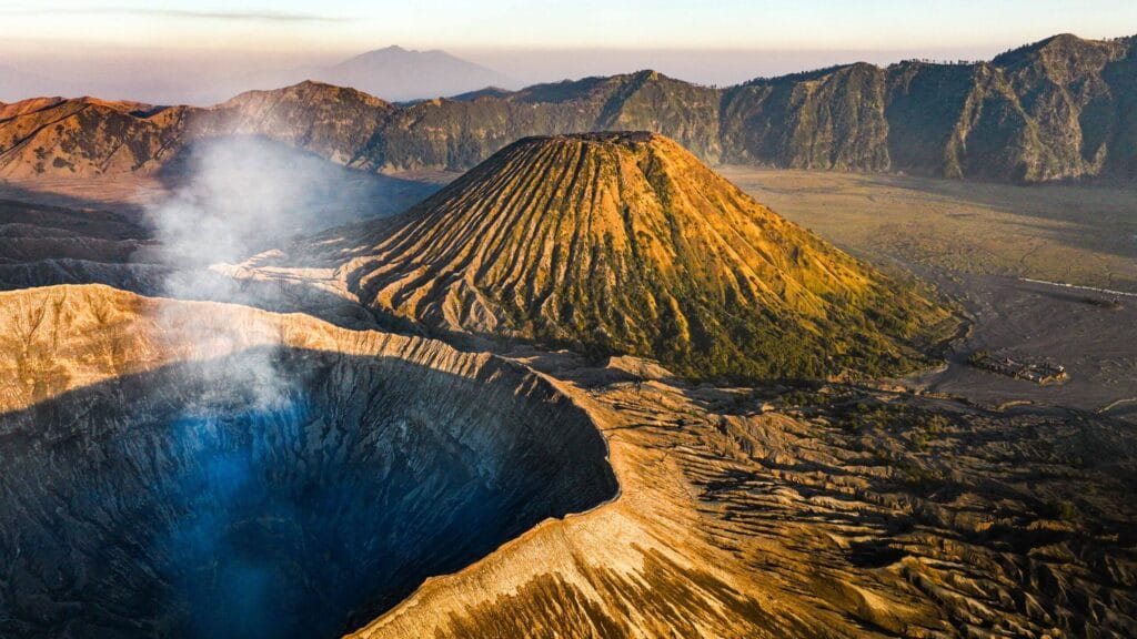 A breathtaking aerial view of Mount Bromo’s crater and surrounding mountains during sunrise, showcasing the volcanic landscape travelers will see when learning how to get to Mount Bromo from Surabaya — a journey filled with stunning natural beauty and adventure.