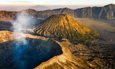 A breathtaking aerial view of Mount Bromo’s crater and surrounding mountains during sunrise, showcasing the volcanic landscape travelers will see when learning how to get to Mount Bromo from Surabaya — a journey filled with stunning natural beauty and adventure.