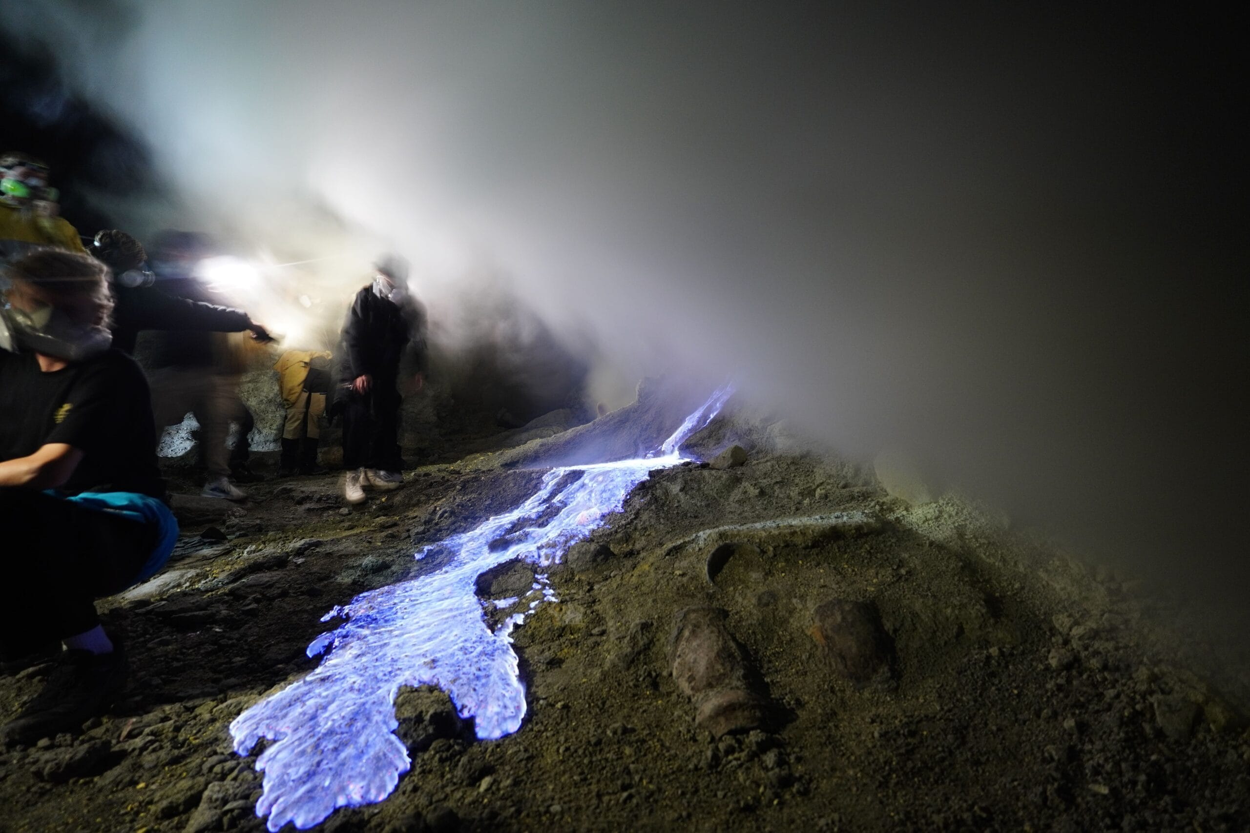 Photographers capturing the glowing sulfur flames at Mount Ijen before sunrise — a perfect example for applying Ijen's Blue Fire Photography Tips to shoot in low light and smoky volcanic conditions.