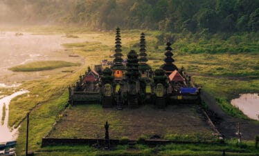 Aerial sunrise view of Ulun Danu Tamblingan Temple surrounded by misty mountains and lake in Bali, Indonesia.