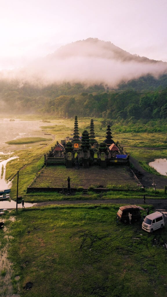 Aerial sunrise view of Ulun Danu Tamblingan Temple surrounded by misty mountains and lake in Bali, Indonesia.