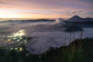 Best Time to Visit Mount Bromo - a sea of clouds covering the valley with glowing village lights below and smoke rising from the volcano’s crater