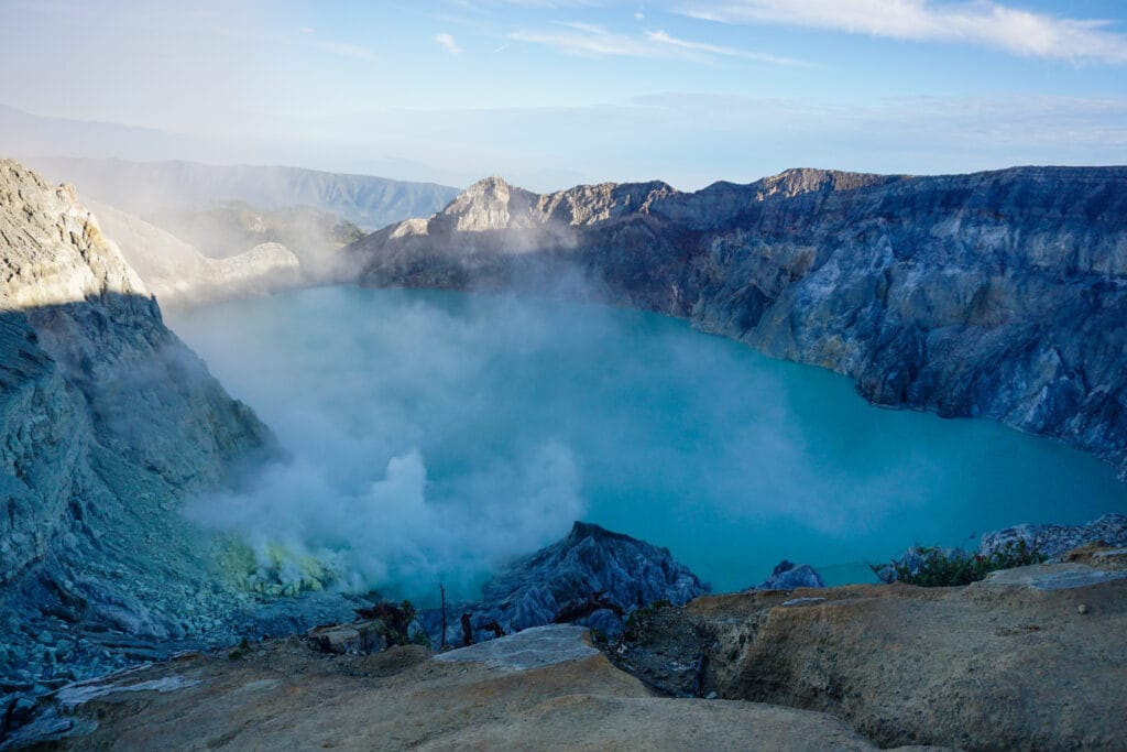 The turquoise crater lake of Mount Ijen surrounded by rocky cliffs and rising sulfur smoke, captured after the Ijen sunrise & Blue Flame.