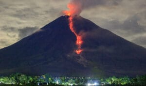 Dramatic night view of an erupting volcano with glowing lava flow streaming down its slope, showcasing the powerful volcanic activity in the Ring of Fire Indonesia.