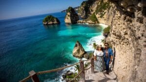 A couple enjoying a scenic cliffside view during their Bali honeymoon, overlooking turquoise waters, dramatic limestone cliffs, and iconic rock formations at a stunning tropical beach.