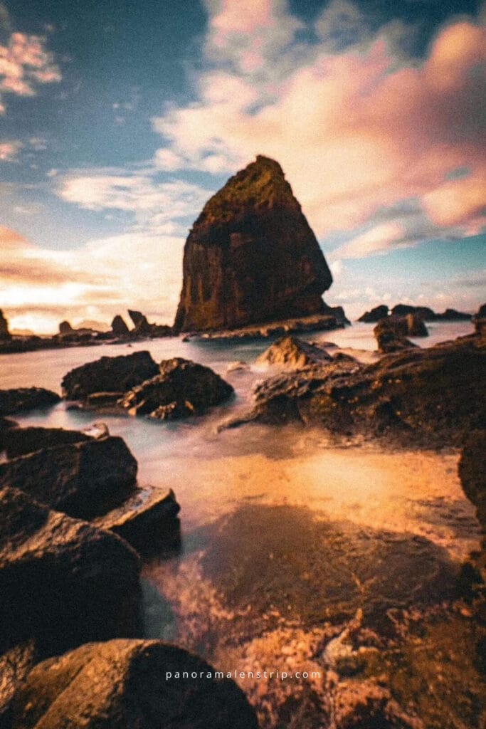 Papuma Beach at sunset featuring iconic rock formation, smooth long-exposure waves, and golden light reflecting on volcanic rocks.