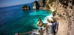 A couple enjoying a scenic cliffside view during their Bali honeymoon, overlooking turquoise waters, dramatic limestone cliffs, and iconic rock formations at a stunning tropical beach.