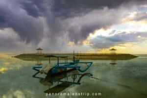 Best beaches in Bali at Sanur Beach with a traditional fishing boat resting on calm shallow water under dramatic sunset clouds
