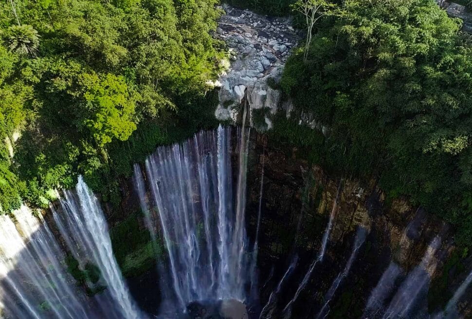 Drone view of Tumpak Sewu Waterfall surrounded by lush green cliffs, showcasing its multi-tiered cascades for a Tumpak Sewu Waterfall travel guide.