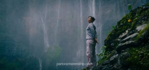 Woman standing beneath Tumpak Sewu Waterfall with flowing water