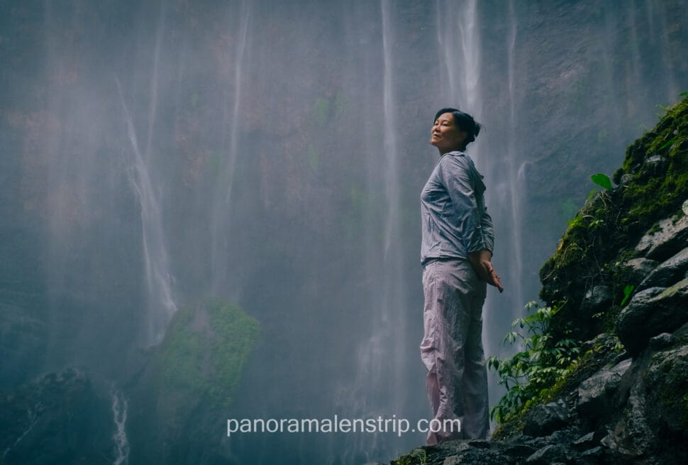 Woman standing beneath Tumpak Sewu Waterfall with flowing water