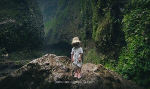 child standing at side viewpoint of Tumpak Sewu waterfall with tall cliffs in background