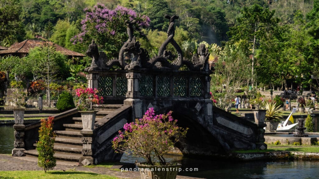 Bali travel tips and tricks featuring Tirta Gangga Water Palace with a traditional stone bridge, lotus ponds, and lush tropical gardens