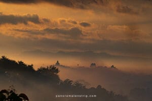 Sunrise view of the Borobudur UNESCO heritage site emerging from morning mist, surrounded by hills and dramatic clouds.