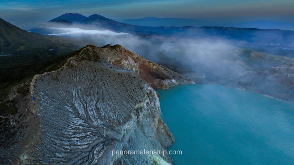 Panoramic aerial view of the turquoise acid crater lake at Mount Ijen, Indonesia, under a morning sky.