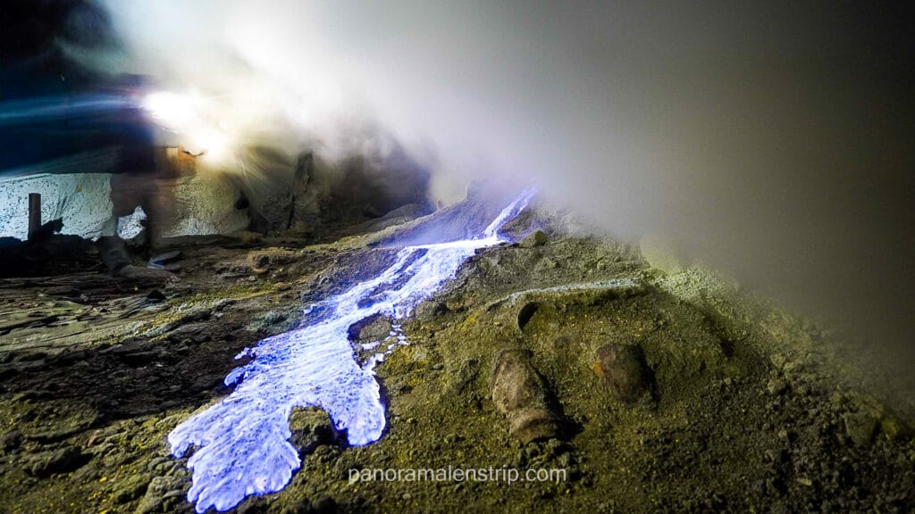 Close-up shot of the electric blue fire flowing like lava over rocky sulfur deposits at night in Ijen Crater.