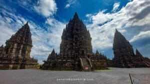 History of Prambanan Temple shown through the main Shiva shrine and surrounding Hindu towers under a dramatic blue sky in Central Java, Indonesia.