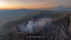 Panoramic landscape of Bromo Tengger Semeru National Park at dawn with soft pastel colors and sea of sand.