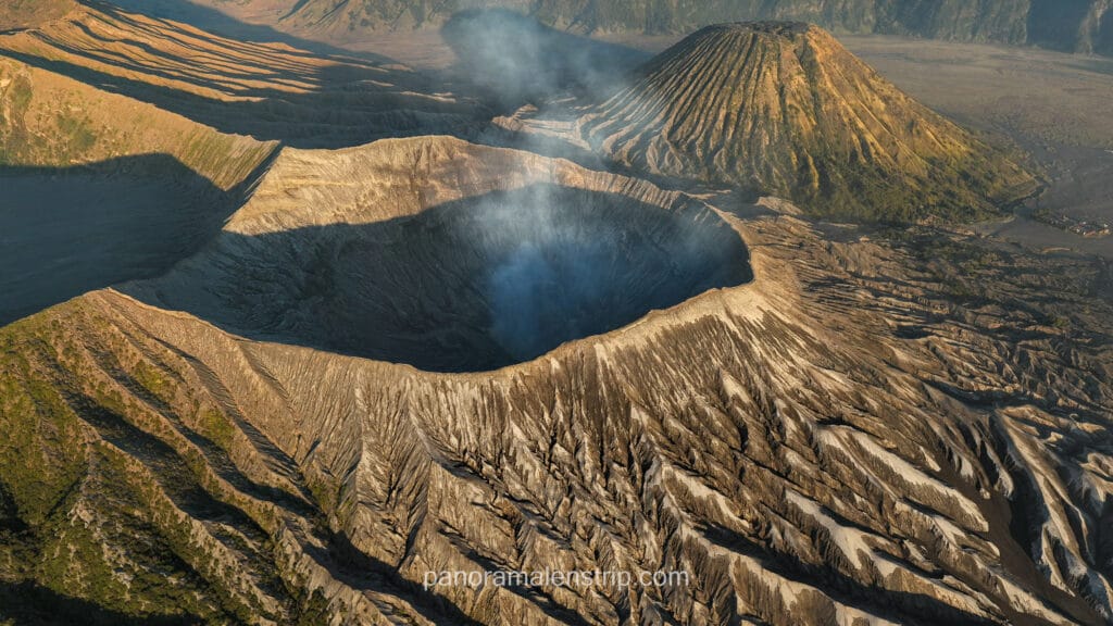 Aerial close-up view of Mount Bromo's smoking crater and the textured slopes of Mount Batok at sunrise.