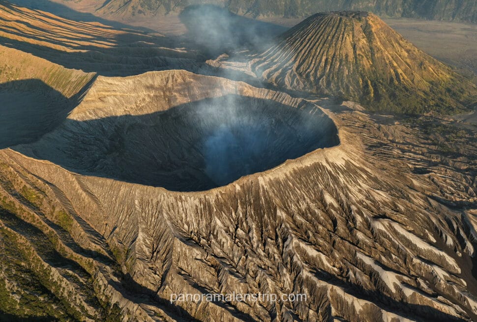 Aerial close-up view of Mount Bromo's smoking crater and the textured slopes of Mount Batok at sunrise.