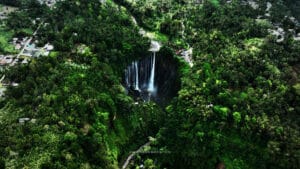 Tumpak Sewu waterfall hike difficulty shown from aerial view, highlighting steep cliffs, jungle terrain, and the dramatic multi-stream waterfall in East Java, Indonesia.