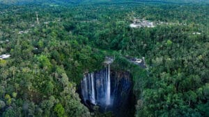 Tumpak Sewu photography capturing a wide aerial view of Tumpak Sewu Waterfall surrounded by dense tropical forest in East Java, Indonesia, highlighting the dramatic cliff, vertical waterfall drop, and lush green landscape from above.