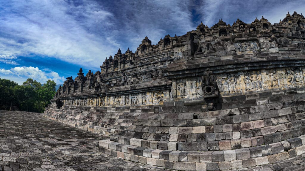 Borobudur Temple Climb showing detailed stone relief panels and upper terrace walls under dramatic blue sky in Central Java, Indonesia.
