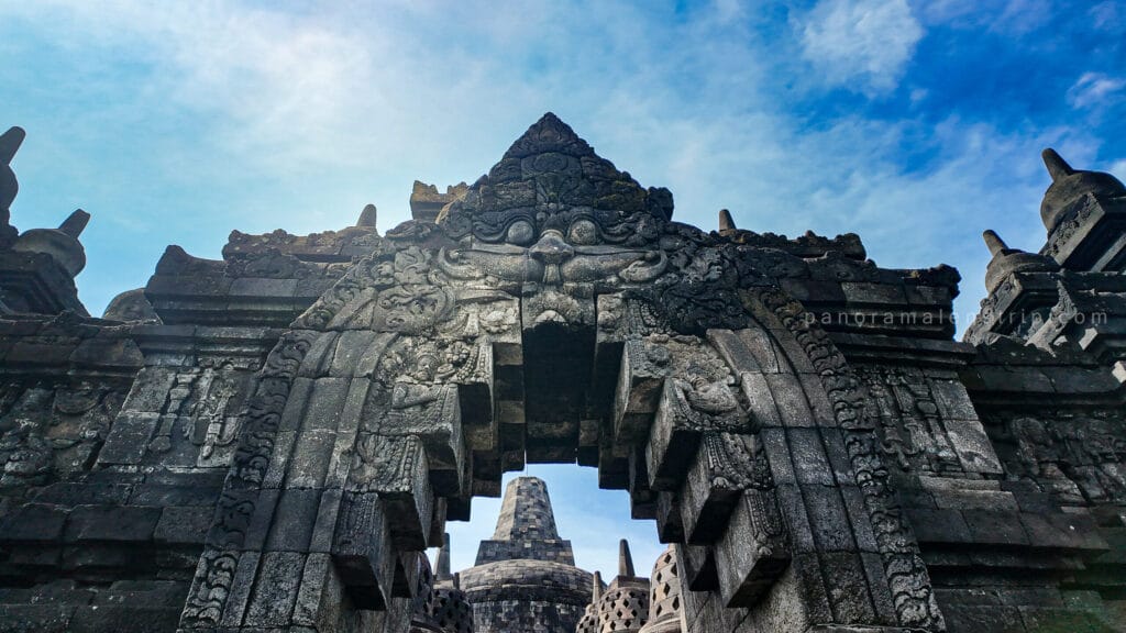 Borobudur sunrise tour architectural detail showing the carved Kala face gate and central stupa at Borobudur Temple beneath a dramatic blue morning sky.