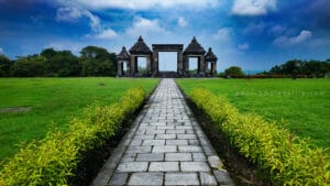 Prambanan photography guide view of symmetrical stone pathway leading to Ratu Boko gate pavilion under dramatic blue sky in Yogyakarta