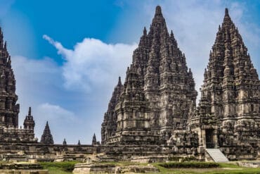 Towering spires of Prambanan Temple rising against a bright blue sky with soft clouds in Yogyakarta, Indonesia