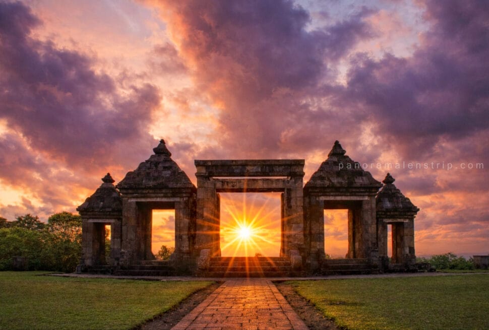 Sunset view through the ancient stone gate of Ratu Boko Temple with dramatic clouds and golden sunlight, highlighting a scenic Ratu Boko tour in Yogyakarta, Indonesia.