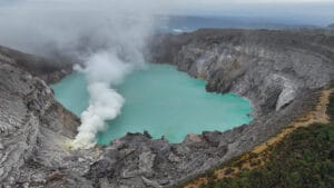 Aerial drone shot of Kawah Ijen crater lake showing active sulfur gas vents and the steep rocky walls of the caldera.