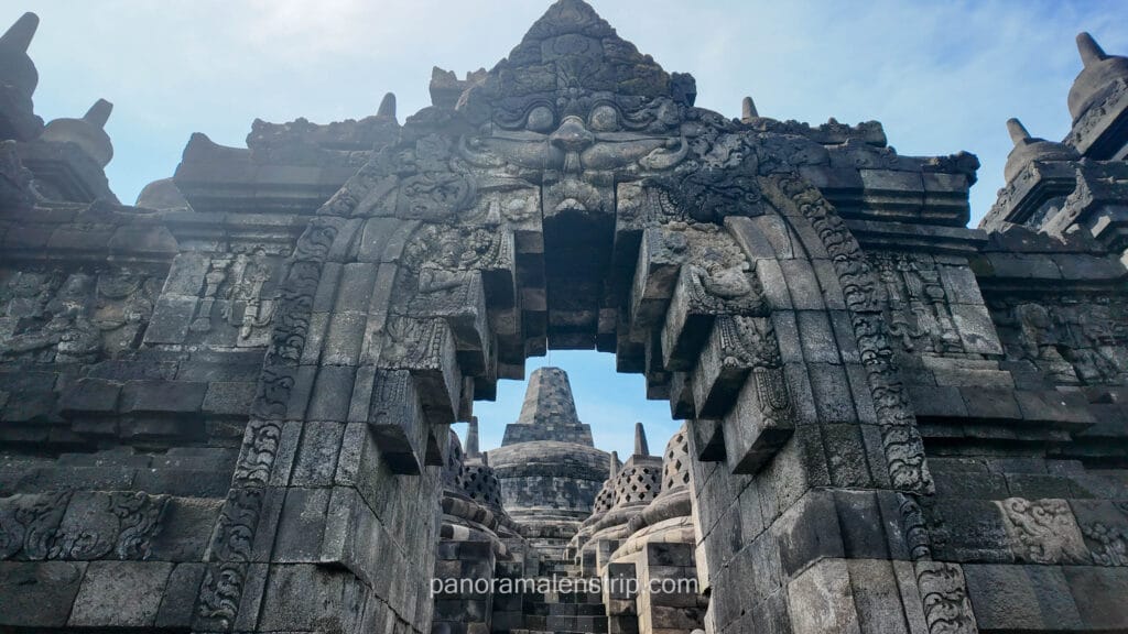 An intricate stone archway with a Kala head carving framing a central stupa at Borobudur Temple.