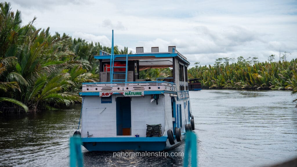 Rear view of a white and blue klotok houseboat with "Save the Nature" text on its deck.