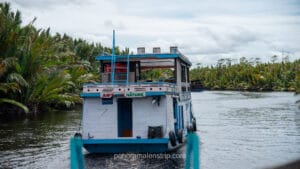 Rear view of a white and blue klotok houseboat with "Save the Nature" text on its deck.