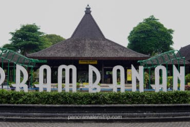Large white letters spelling "PRAMBANAN" in front of a traditional Javanese joglo-style building at the park entrance.