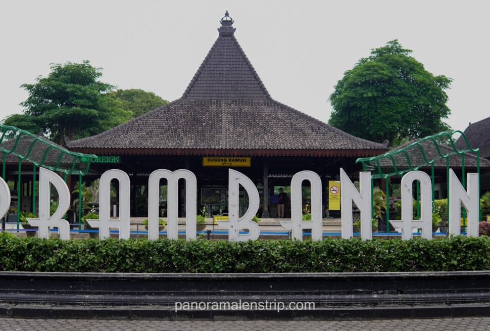 Large white letters spelling "PRAMBANAN" in front of a traditional Javanese joglo-style building at the park entrance.