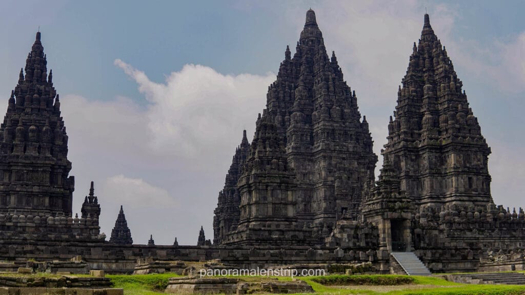 The three main Trimurti temples of Prambanan standing majestically against a blue sky with white clouds.