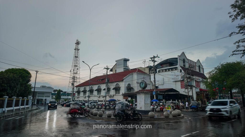 Zero Kilometer Point intersection in Yogyakarta on a rainy evening with the historic Post Office building and a communication tower.