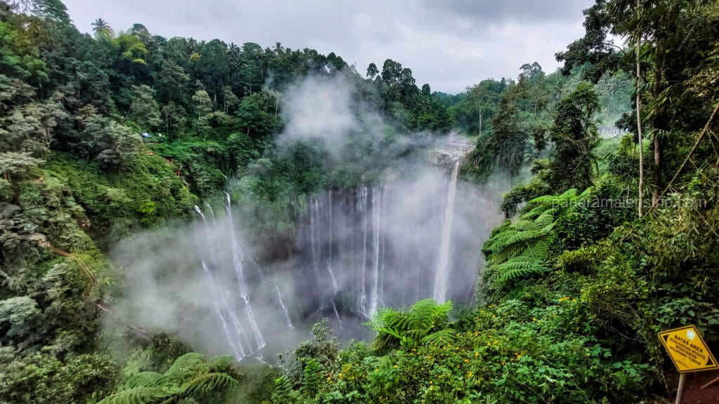 Wide angle view of Tumpak Sewu Waterfall from the panorama viewpoint on a misty, overcast day.