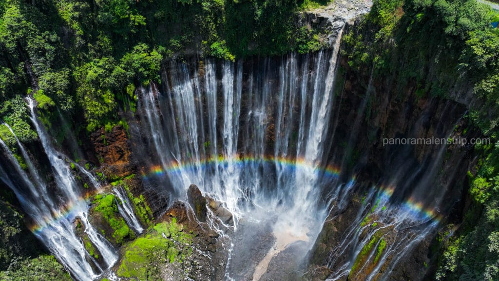 Drone shot of Tumpak Sewu Waterfall in East Java showing a vibrant rainbow across the curtain-like falls.