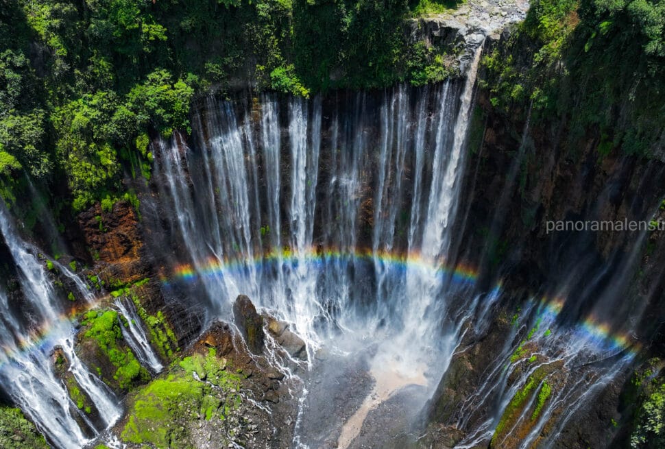 Drone shot of Tumpak Sewu Waterfall in East Java showing a vibrant rainbow across the curtain-like falls.