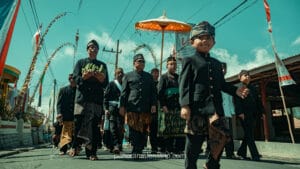 Tenggerese villagers in traditional black attire and udeng walking in a cultural procession beneath a ceremonial umbrella.