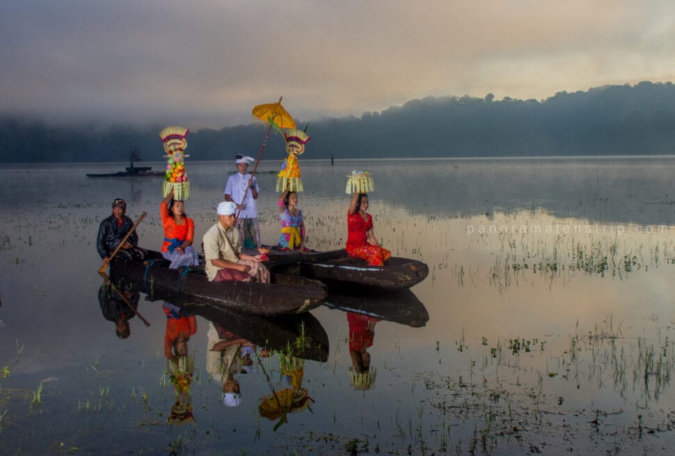 Balinese women carrying colorful offerings while riding traditional boats on Tamblingan Lake during a cultural ceremony, one of the unique bali photography spots.