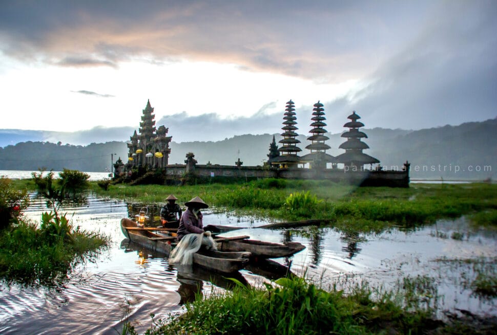 Traditional wooden boat with fishermen on Tamblingan Lake at sunrise with ancient temple and misty mountains, one of the most scenic bali photography spots.