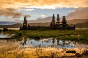 Ancient temple with multi-tiered pagodas at Tamblingan Lake during golden sunrise reflection, one of the most scenic bali photography spots.