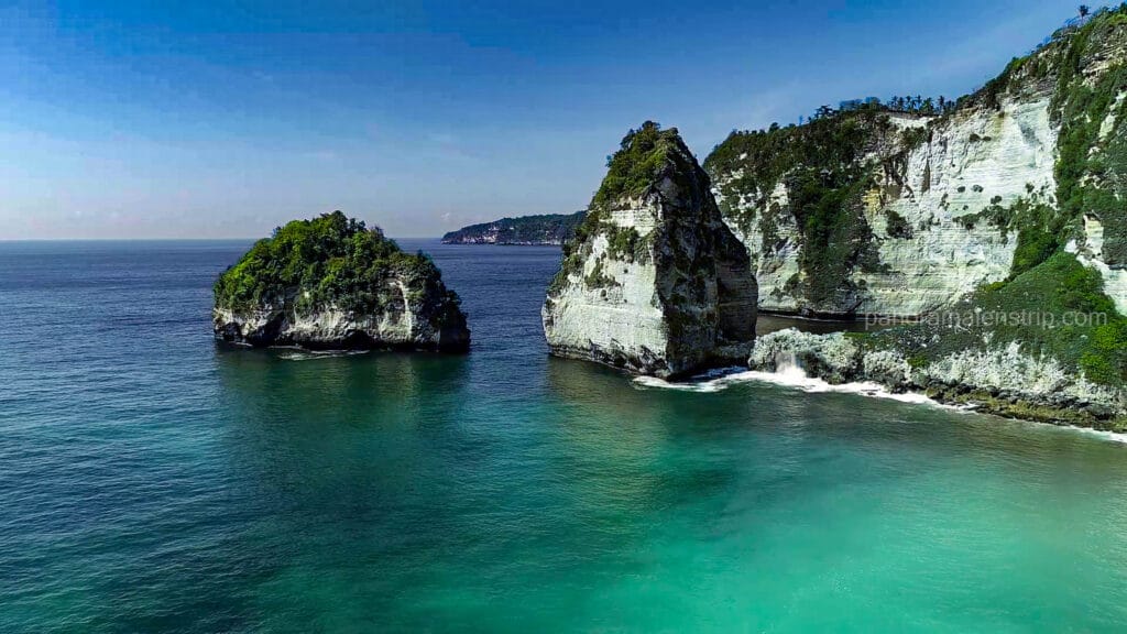 Aerial view of green-topped limestone rock formations rising from bright turquoise ocean waters off the coast of Nusa Penida, Bali.