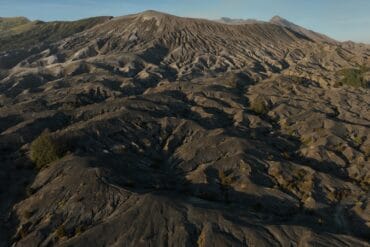 Wide aerial view of Indonesia's Pasir Berbisik, a vast volcanic sand sea with eroded hills and distant mountains.